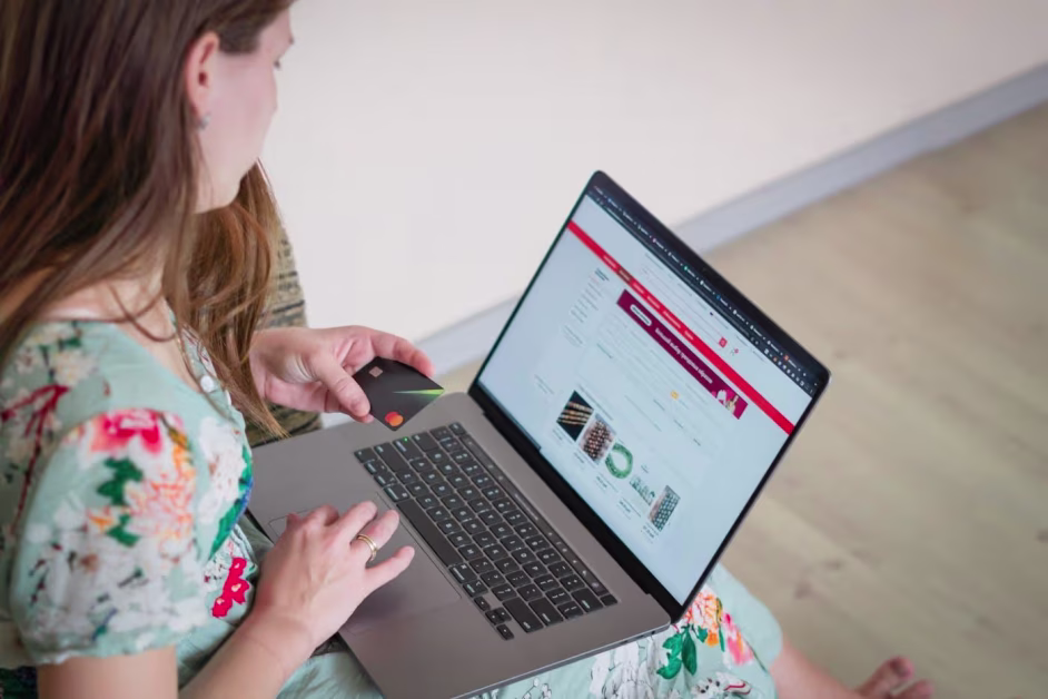 Femme assise de profil utilisant un ordinateur portable et tenant une carte bancaire noire pour effectuer un paiement en ligne.