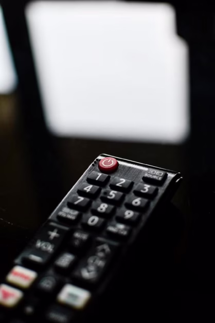 Une télécommande noire posée sur une surface sombre, mettant en valeur le bouton rouge d'alimentation.