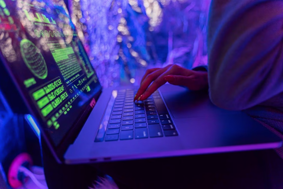Main d'une personne tapant sur le clavier d'un ordinateur portable affichant des lignes de code vertes.