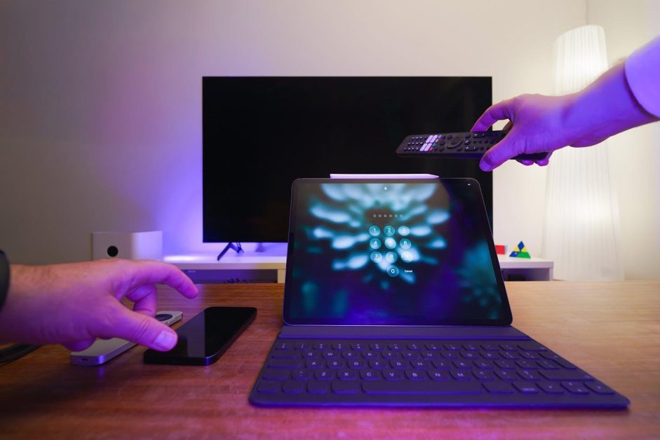 Une tablette avec clavier affichant un écran de verrouillage à code numérique, avec une main tenant une télécommande au-dessus d'elle.