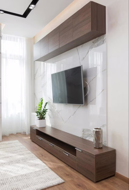 Grand écran de télévision fixé sur un mur en marbre blanc au-dessus d'un meuble bas en bois dans un salon lumineux.