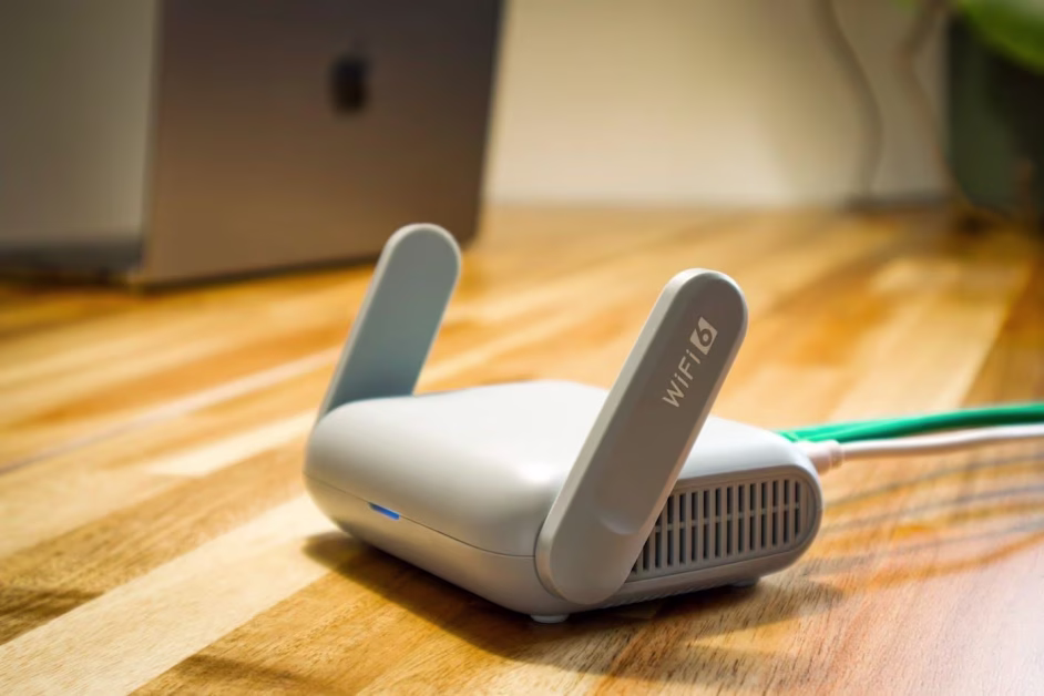 Un modem ou routeur internet blanc compact avec l'inscription Wi-Fi 6 sur ses antennes, posé sur un bureau en bois.
